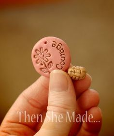 a hand holding a small pink button with words on it