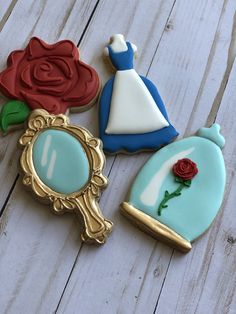 three decorated cookies sitting on top of a white wooden table next to a mirror and a rose