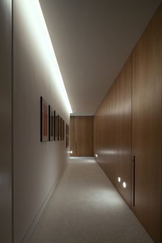 an empty hallway with wooden cabinets and lights on the side wall, leading to another room