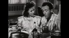 a man and woman sitting at a table with cups in front of them, looking at each other