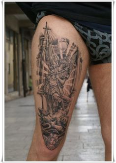 a man with a tattoo on his leg is standing in front of a building and holding a cross