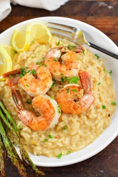 shrimp and grits with asparagus on a white plate next to lemon wedges