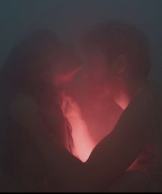 two people are kissing in the dark with red light coming from behind their heads and arms