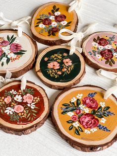 four wooden slices with flowers painted on them and tied in white ribbon around the edges