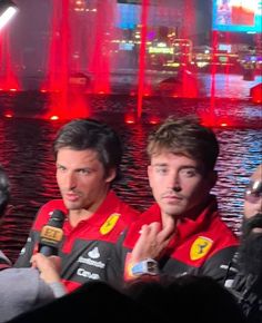 two men standing next to each other in front of a fountain with red lights on it