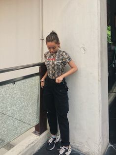 a woman leaning against a wall with her hand on her hip and looking down at the ground