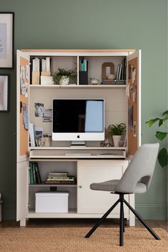 a desk with a computer on it and a chair next to it in front of a green wall