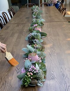 a long table with succulents and greenery on it, along with a brush