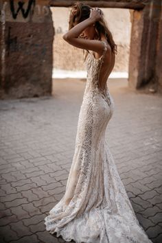 a woman in a wedding dress standing on a brick floor with her arms behind her head