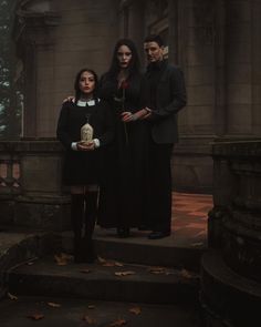 three people standing on steps in front of an old building, one holding a rose