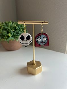 the jack and sally earrings are hanging on a stand next to a potted plant