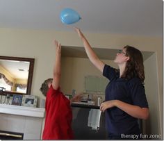 two people in a living room playing with a frisbee and another person reaching up to catch it