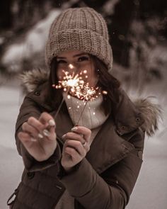 a woman holding sparklers in her hands while wearing a winter hat and coat with fur collar