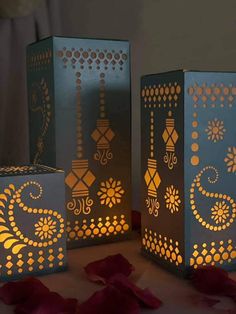 three paper lanterns with designs on them sitting on a table next to red rose petals