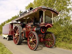 an old fashioned steam engine driving down the road in front of some bushes and trees