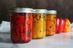 four jars filled with different colored peppers on top of a white counter next to each other