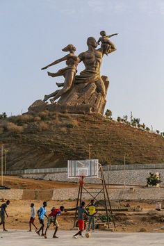 several people playing basketball in front of a large statue on top of a hill,