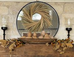 a wreath on top of a mantle next to two candles and some gourds