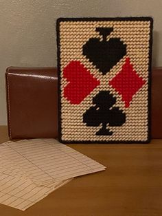 a knitted playing card sitting on top of a wooden table next to a wallet