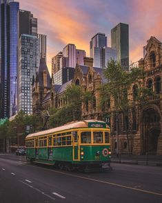 a green and yellow trolley car driving down the street in front of some tall buildings