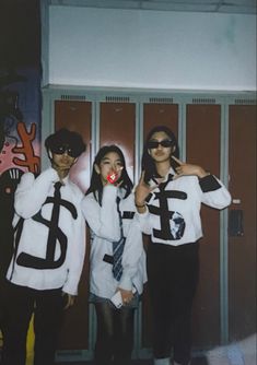 three people posing for a photo in front of lockers with letters painted on them