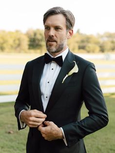 a man in a tuxedo is adjusting his bow tie and looking at the camera