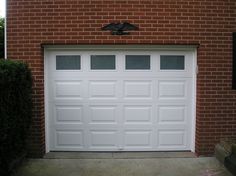 a white garage door in front of a red brick building with an eagle on the top