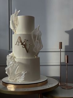 a three tiered white wedding cake with flowers and initials on the top, sitting on a table