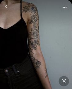 a woman's arm with flowers and leaves tattooed on her left arm, in front of a white wall