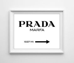 a white framed poster with the words prada marfa and an arrow pointing to it