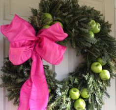 a wreath with green apples and pink ribbon hanging on the front door to give it a festive touch