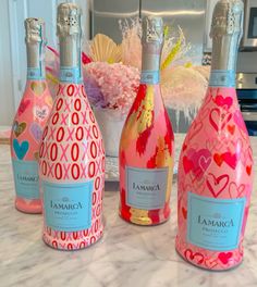 three bottles of pink and blue wine on a marble counter with flowers in the background