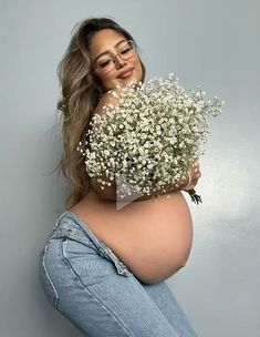 a pregnant woman with glasses holding a bouquet of baby's breath flowers in front of her stomach