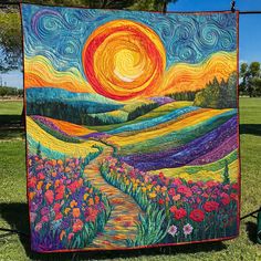 a quilt hanging on a clothes line in the grass with flowers and trees around it