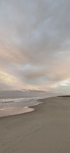 a person walking on the beach with a surfboard in their hand and clouds in the background