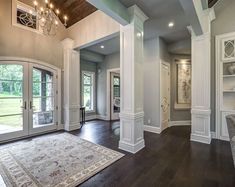 a large living room with wood floors and white columns on the ceiling, along with french doors that lead to an outdoor patio