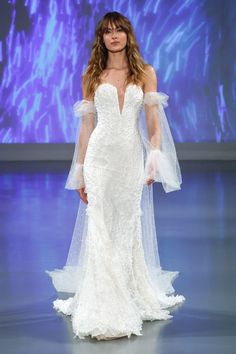 a model walks the runway in a white gown with sheer sleeves and long veils