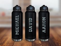 three black water bottles sitting on top of a wooden table