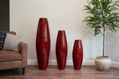 three red vases sitting on top of a wooden floor next to a brown chair