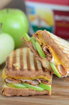 a sandwich cut in half sitting on top of a cutting board next to an apple