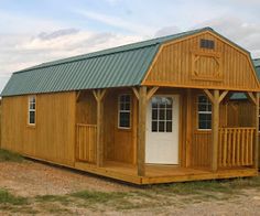 a small wooden building sitting on top of a dirt field next to a green roof