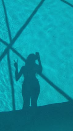 the shadow of a person standing in front of a swimming pool with their hand up