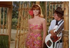 two people standing next to each other in front of a bamboo structure holding guitars and an electric guitar