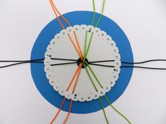 a white clock with orange and green wires connected to it on a blue circular surface