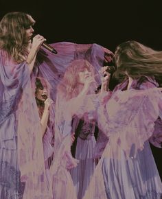 three women in purple dresses singing on stage