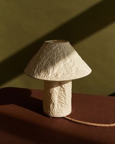 a white lamp sitting on top of a table next to a red cloth covered wall