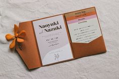 an orange and white wedding card with a flower on the front is laying on a bed