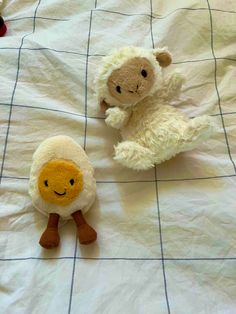 two stuffed animals sitting on top of a white sheet covered bed next to each other