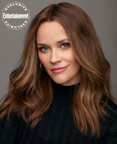 a woman with long hair and blue eyes posing for a photo in front of a gray background