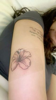 a woman laying down with a tattoo on her arm that has a flower on it